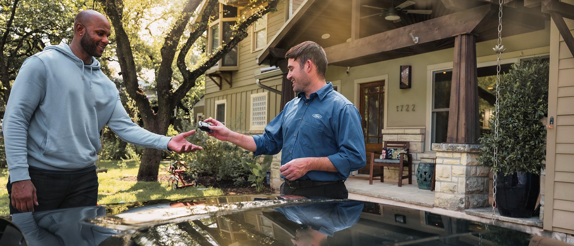 A Ford Service representative hands a Ford owner’s keys back to them in the driveway of their home.