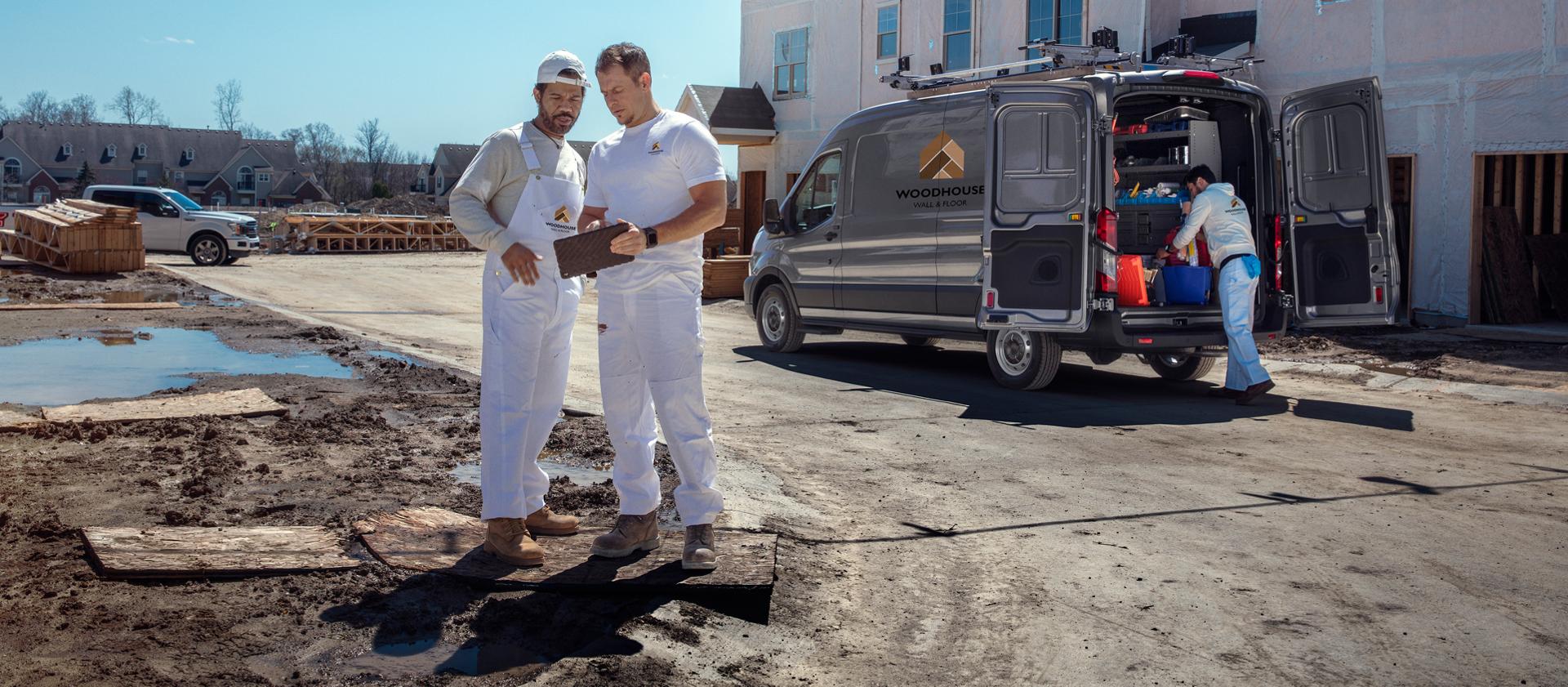 Two painters review a tablet next to their 2027 Ford Transit® van at a construction site