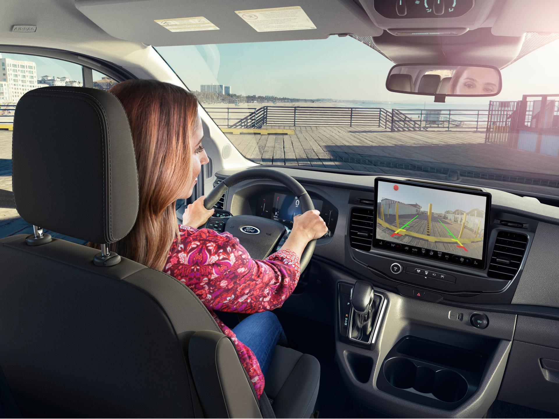 Woman in 2027 Ford Transit® van using rearview camera display with parking sensors