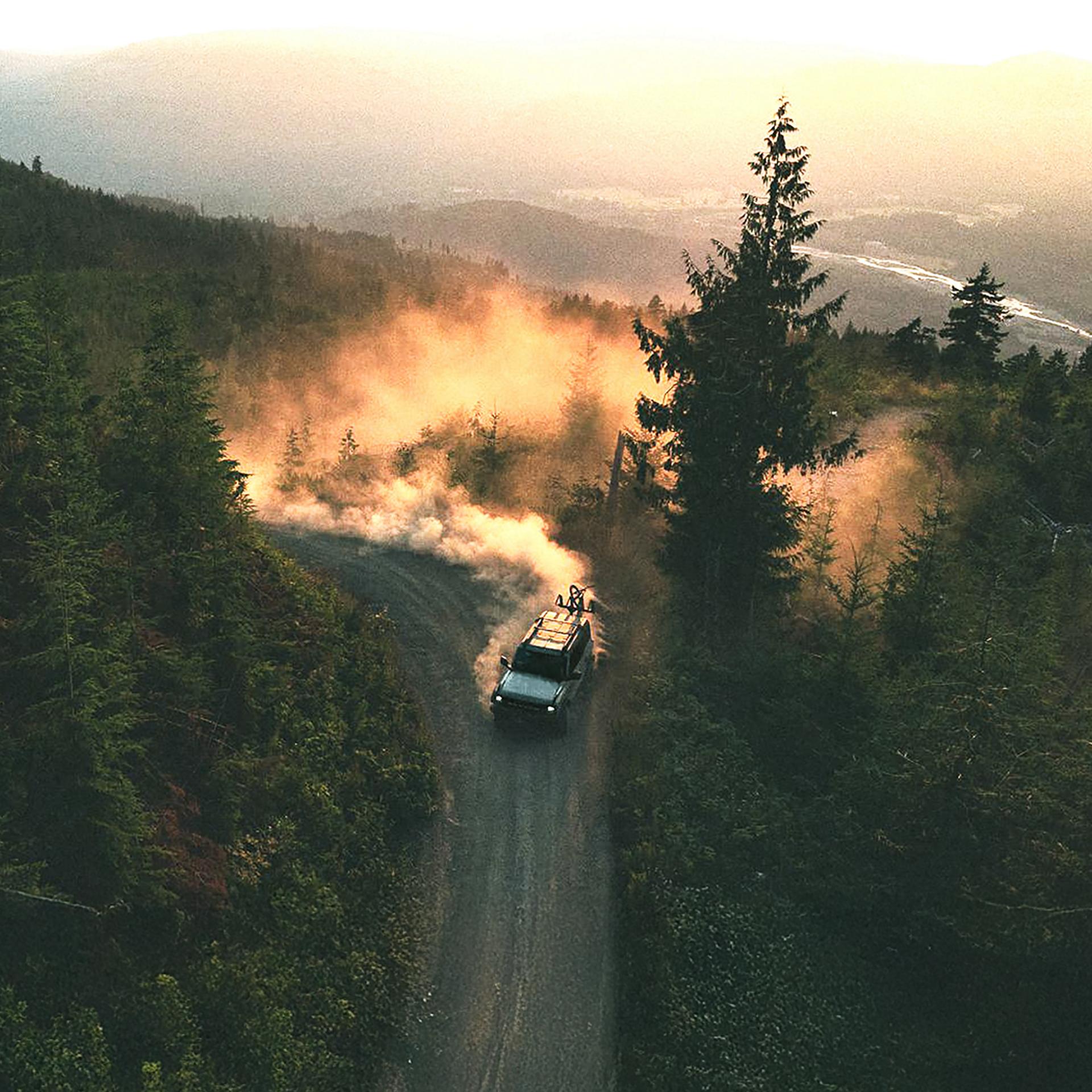 A 2026 Ford Bronco® SUV kicking up dust on a winding hillside trail at sunset