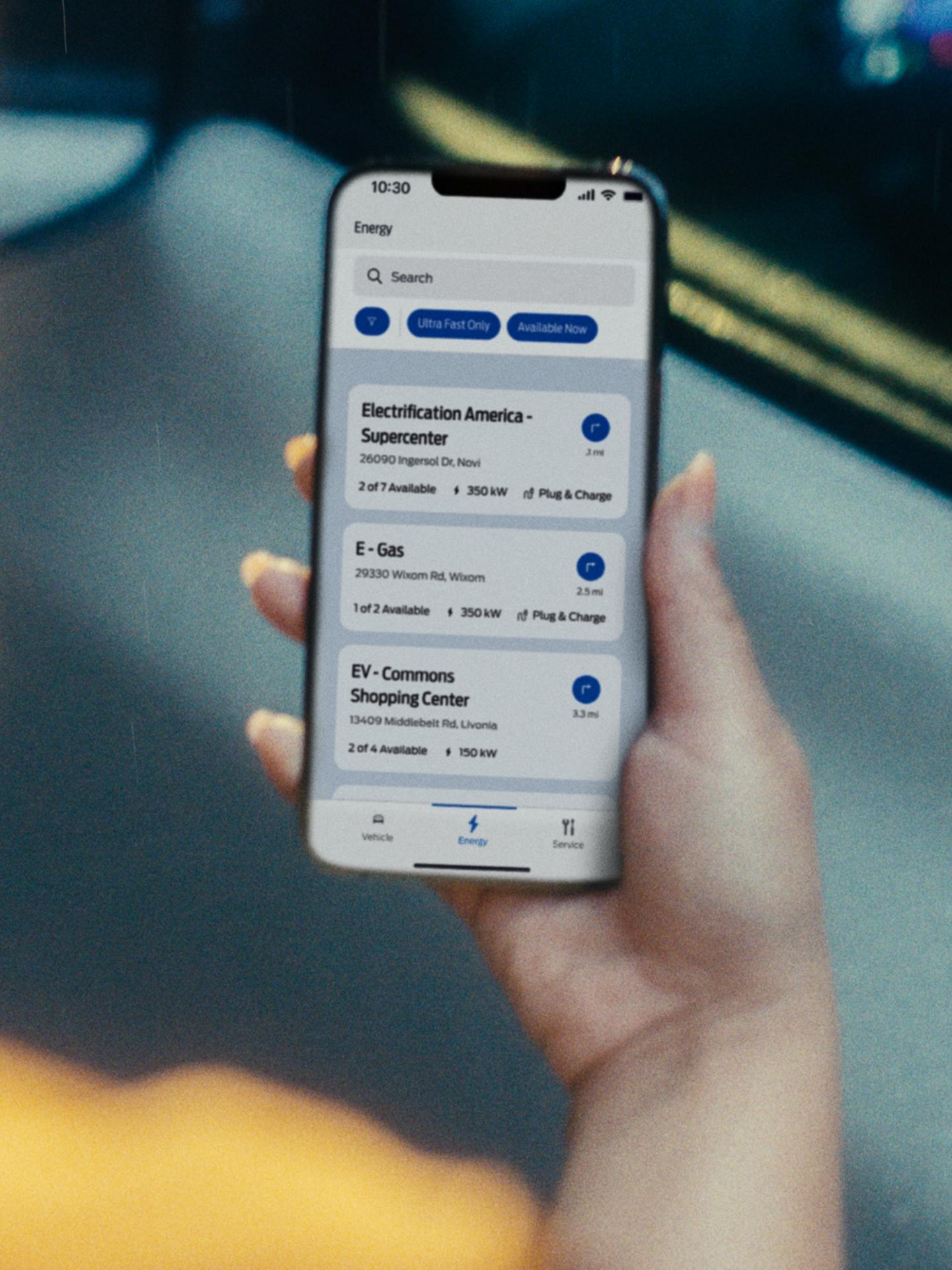 Person holding a smart phone displaying public charging information.