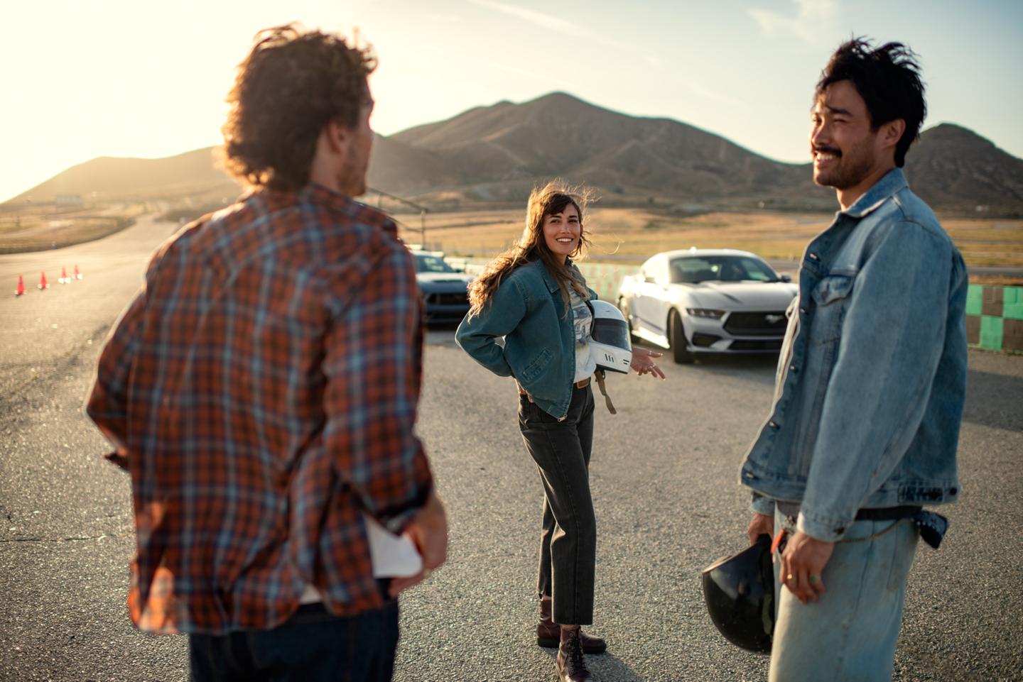 People gathered at a racetrack with Mustang vehicles in the background.