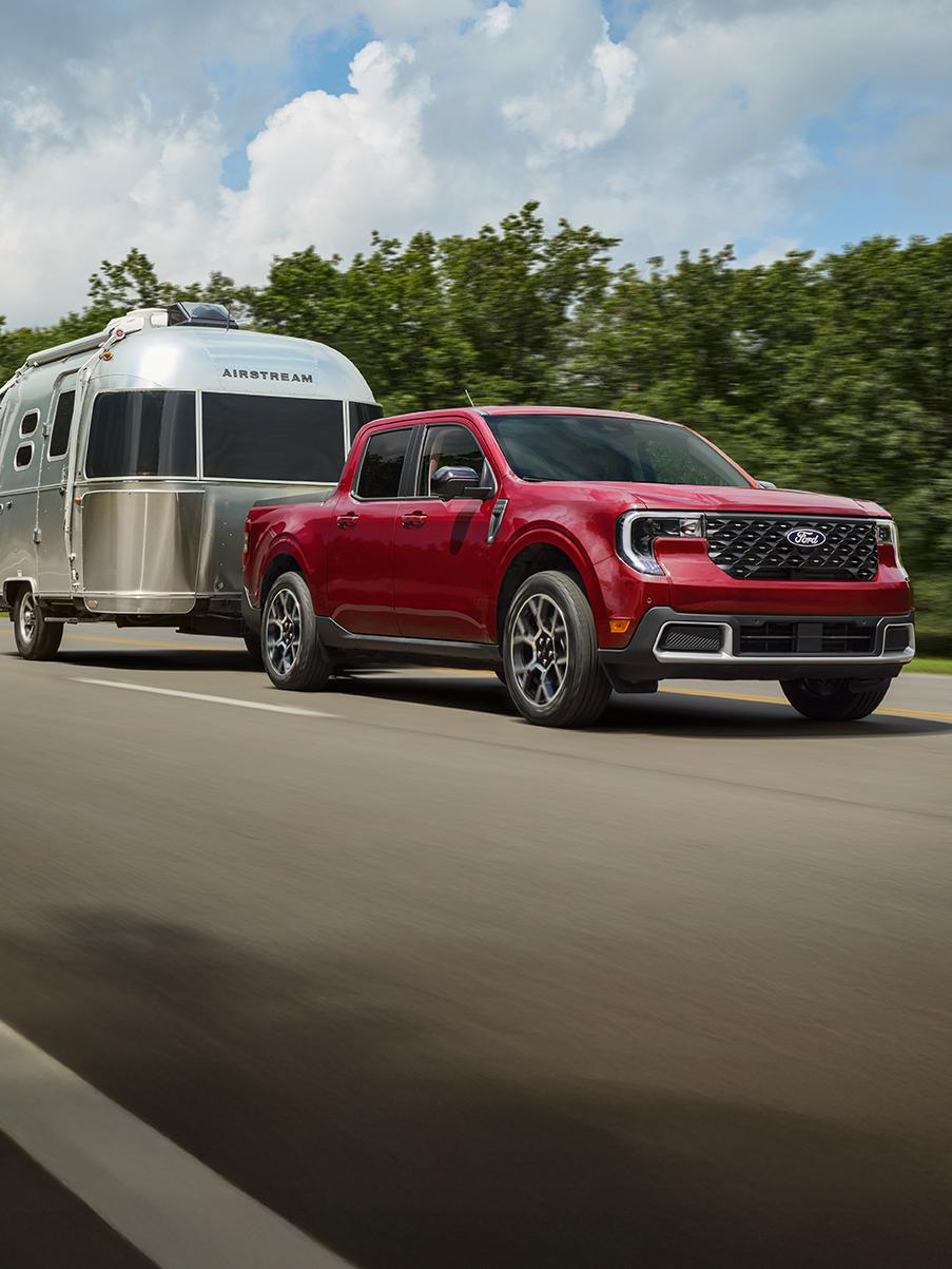 Red Maverick driving on a highway and towing an Airstream trailer.