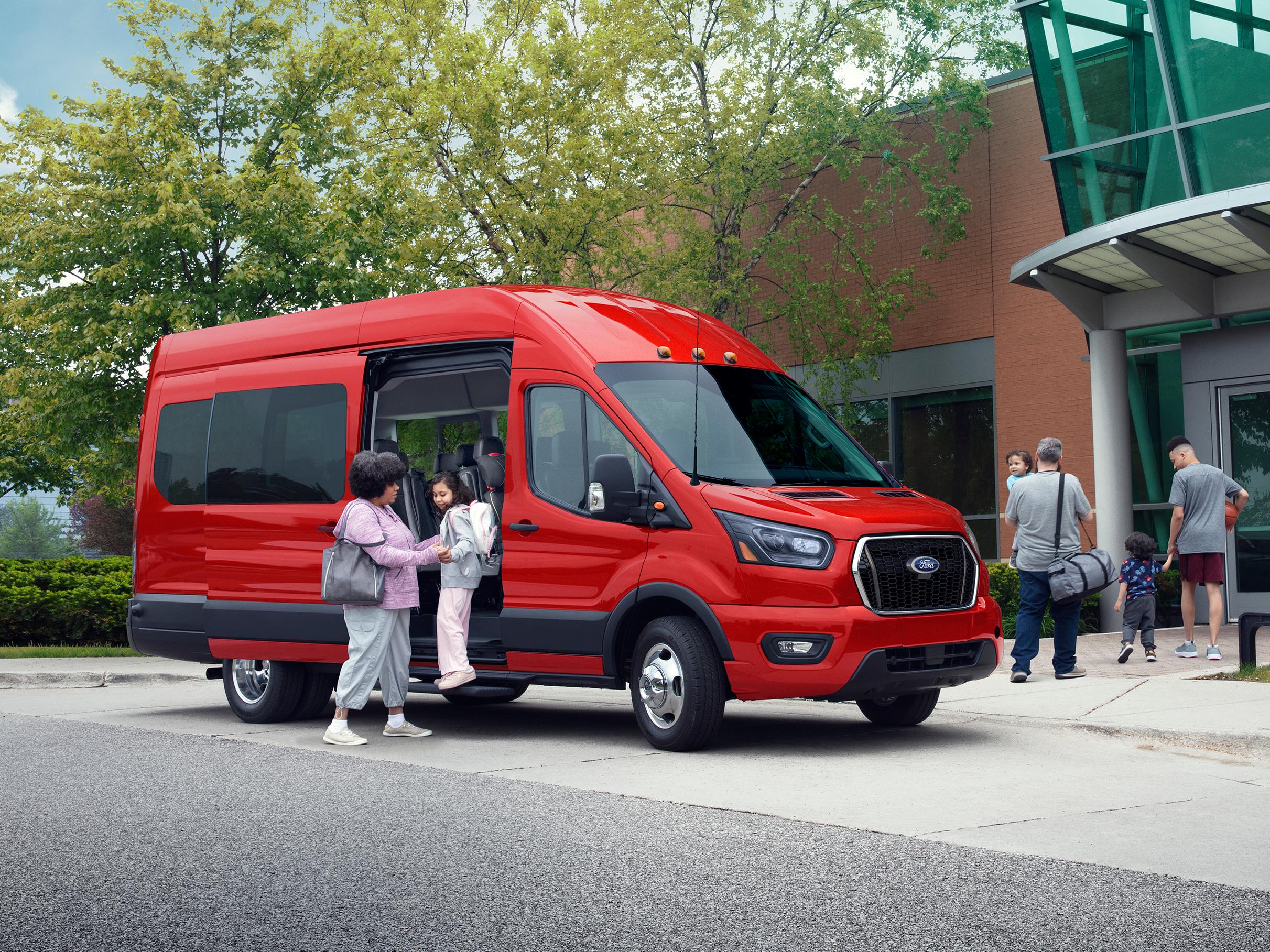 A 2026 Ford Transit® Passenger Van model parked in front of a building with people exiting through the side door