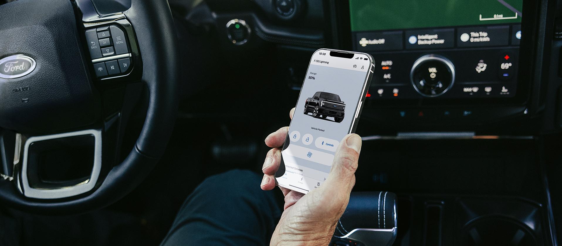 The hand of a driver seated in a 2025 Ford F-150® Lightning® pickup, holding a smartphone showing the FordPass® app