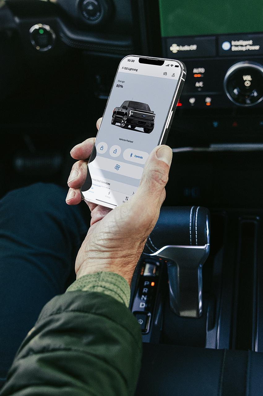 The hand of a driver seated in a 2025 Ford F-150® Lightning® pickup, holding a smartphone showing the FordPass® app
