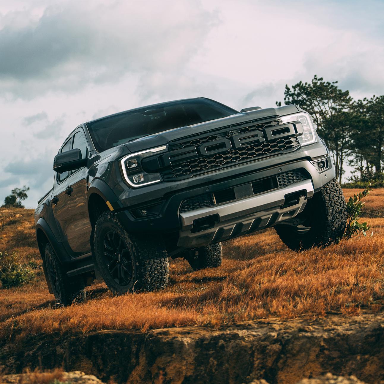 Three-quarter front view of a grey Ford Ranger Raptor off-roading through an open field. 