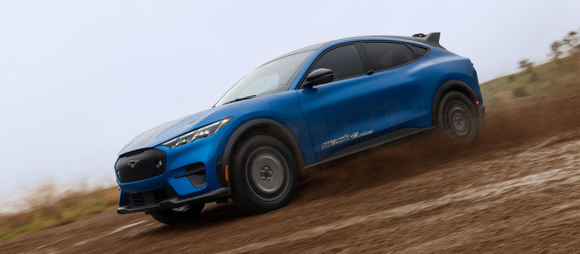 A blue Mustang Mach-E powering through a muddy trail. 