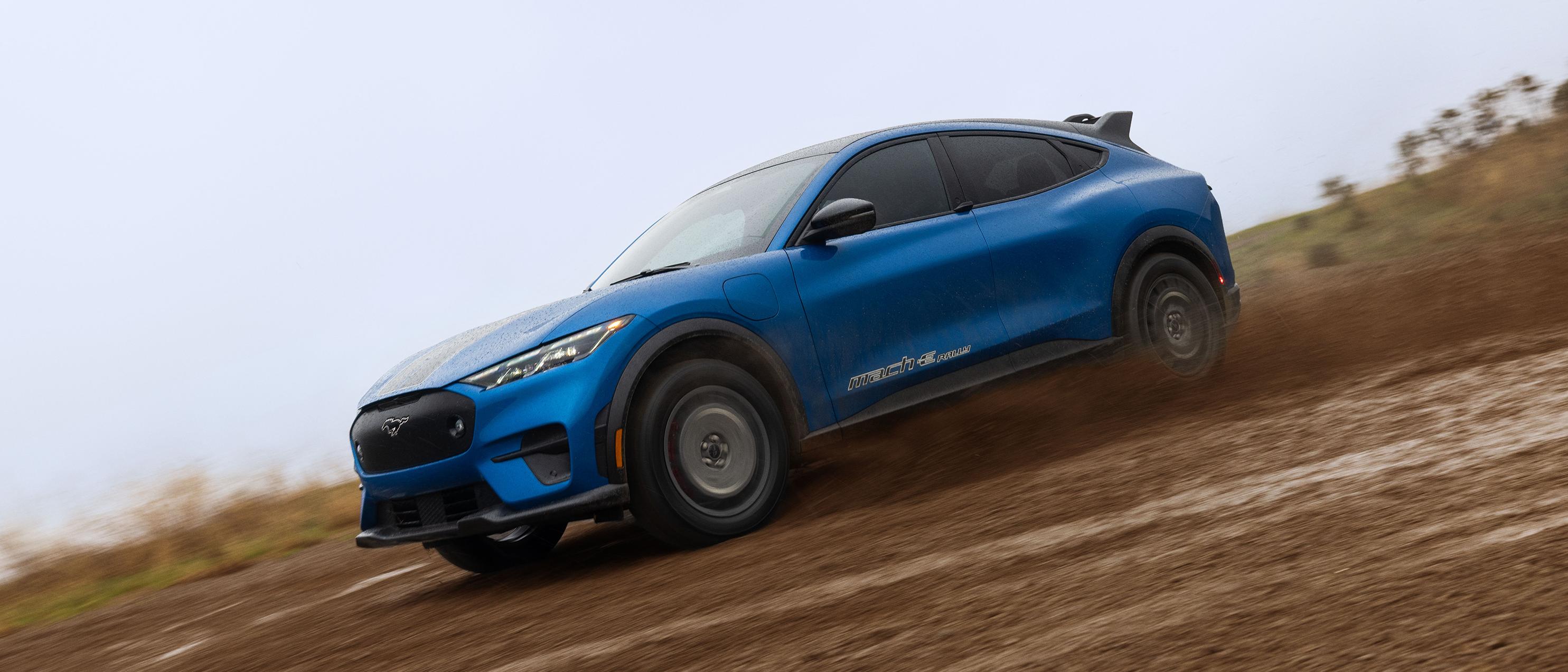 A blue Mustang Mach-E powering through a muddy trail. 