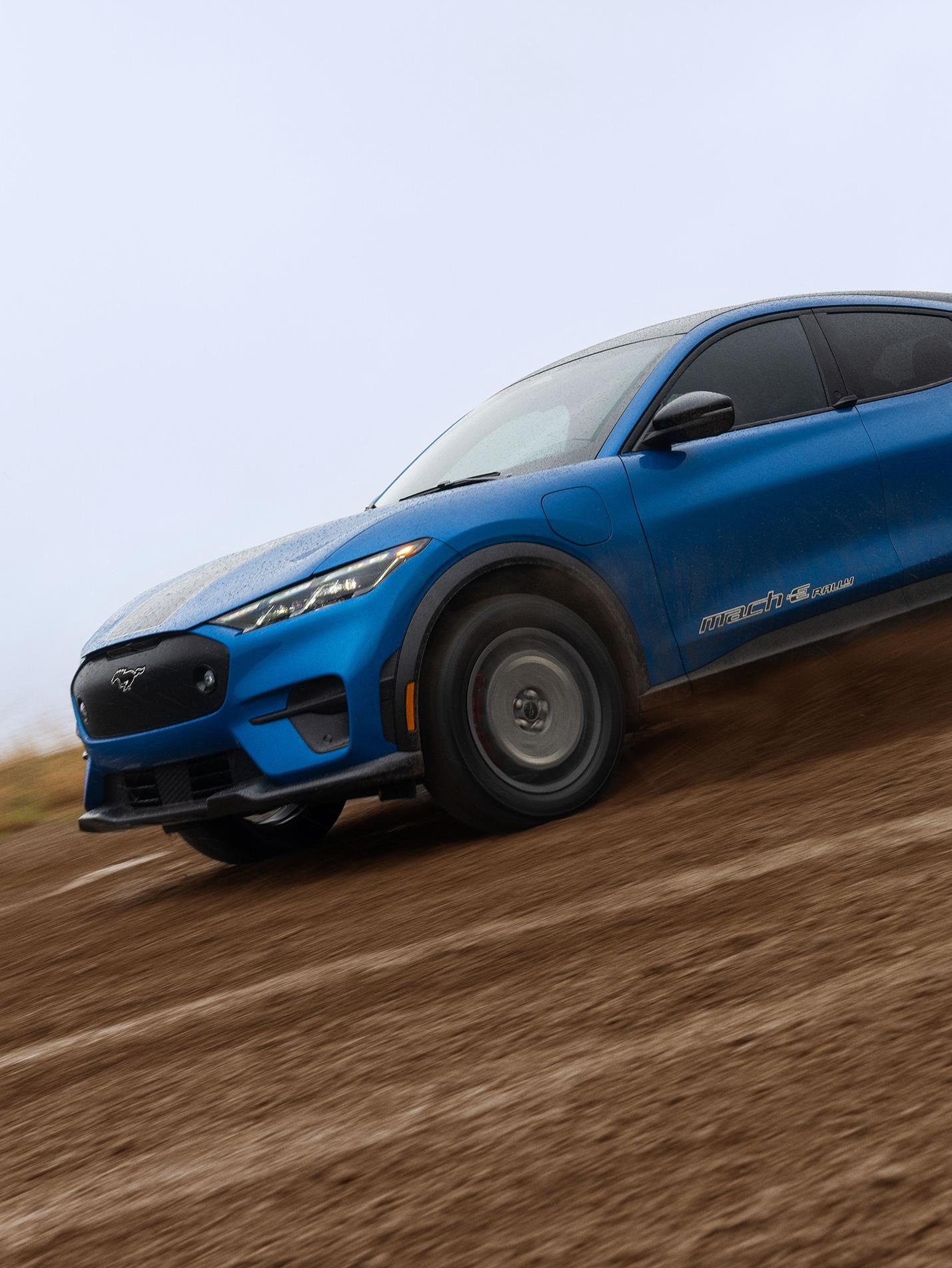 A blue Mustang Mach-E powering through a muddy trail. 