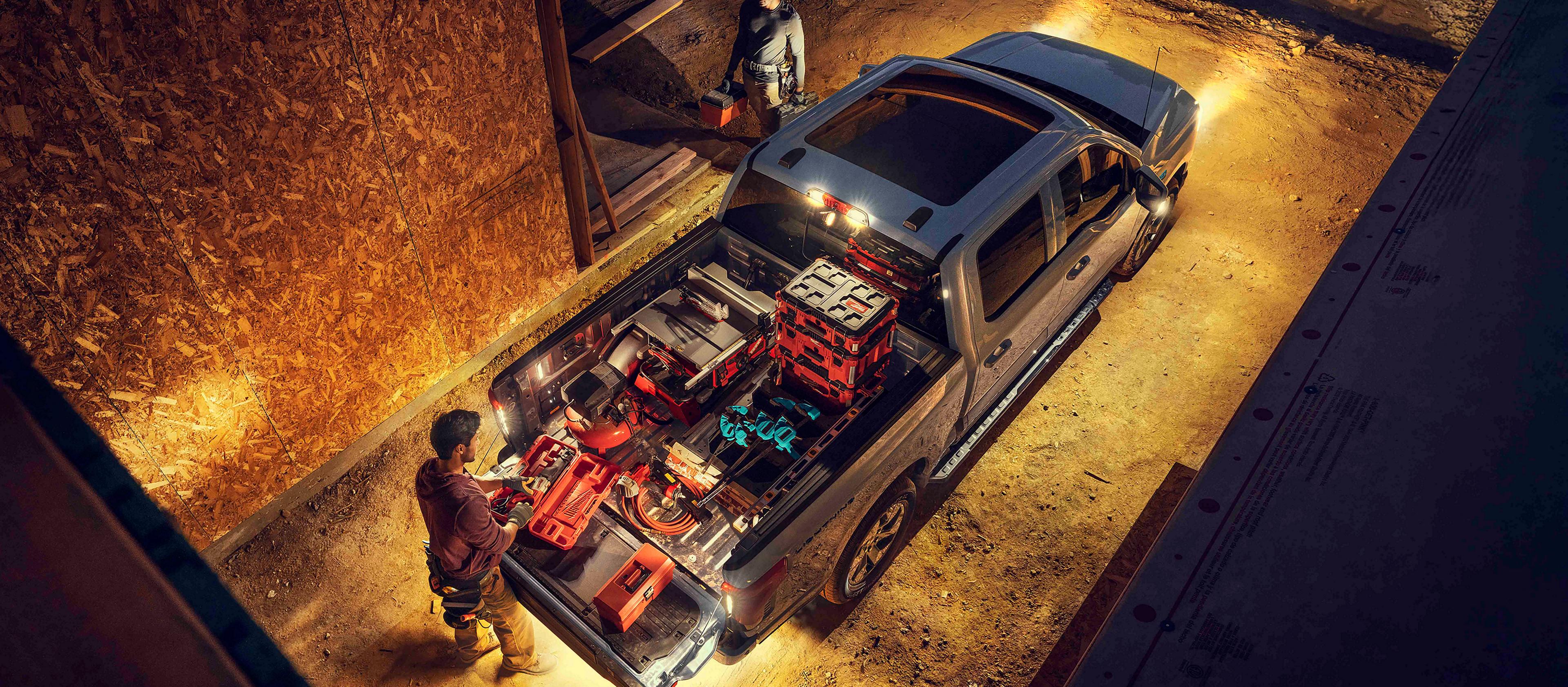 A 2025 Ford F-150® Lightning® lit up at night with a person on a construction site grabbing gear from the truck bed