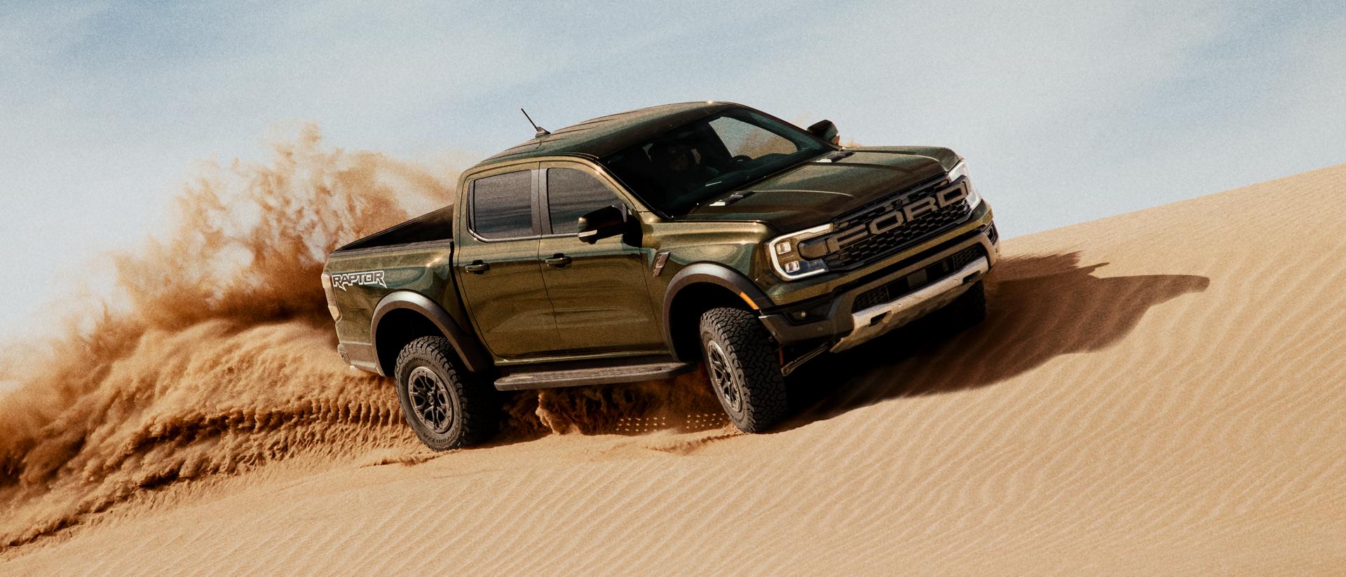 A 2025 Ranger® Raptor® being driven over a sand dune, kicking up sand