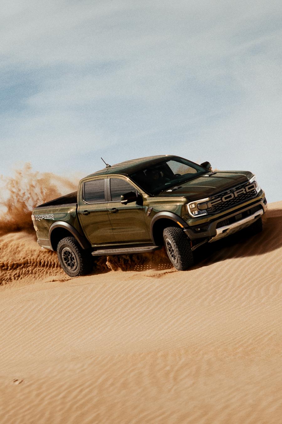 A 2025 Ranger® Raptor® being driven over a sand dune, kicking up sand