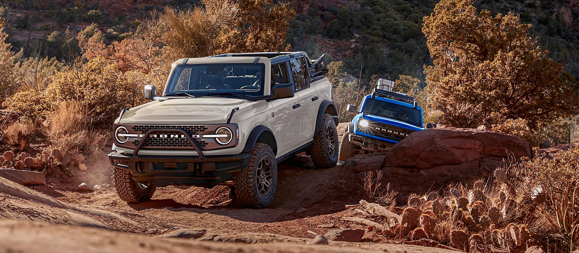 Two 2026 Ford Bronco® SUVs being driven on a scrubby dirt trail