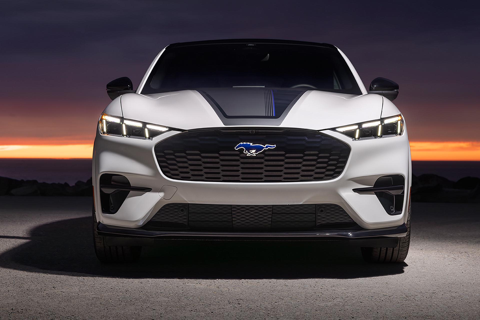 Front end of a 2026 Ford Mustang Mach-E® GT model with hood stripe against a sunset background