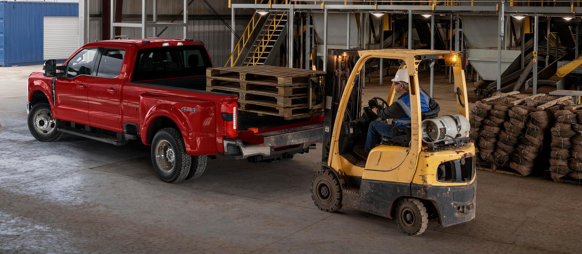 2026 Ford Super Duty® F-350® Lariat® model with the tailgate open while a forklift loads wooden palettes into the truck bed