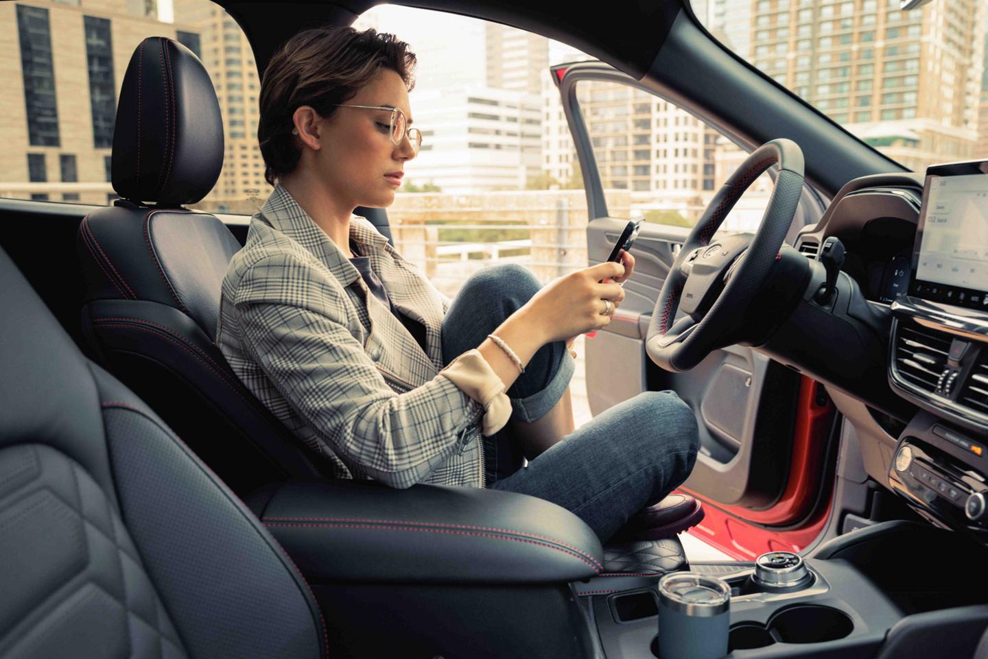 Person holding smartphone sitting in a parked vehicle with the driver side door open