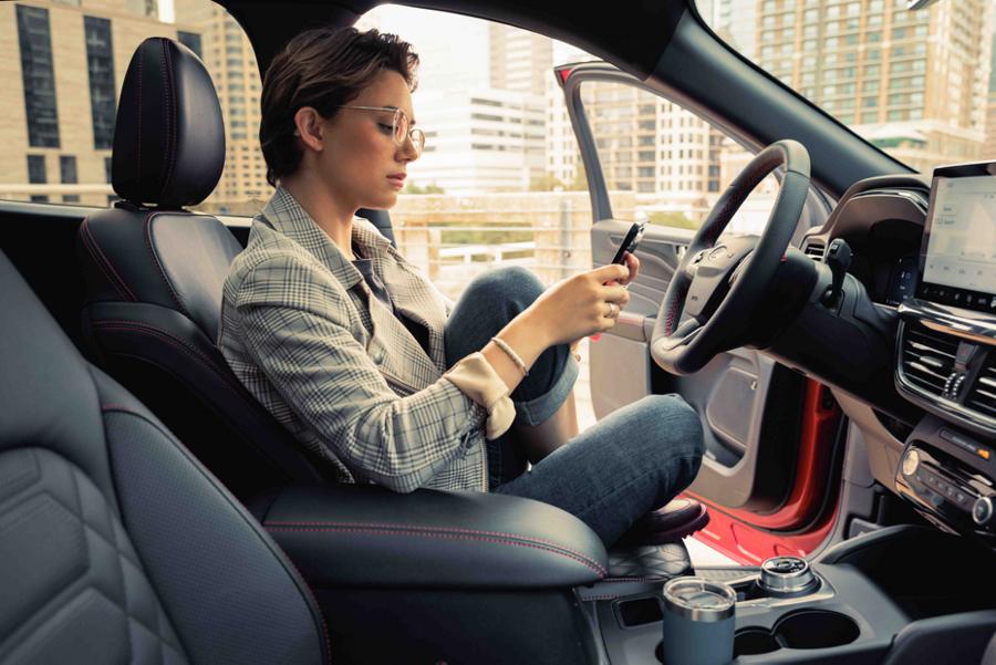 Person holding smartphone sitting in a parked vehicle with the driver side door open