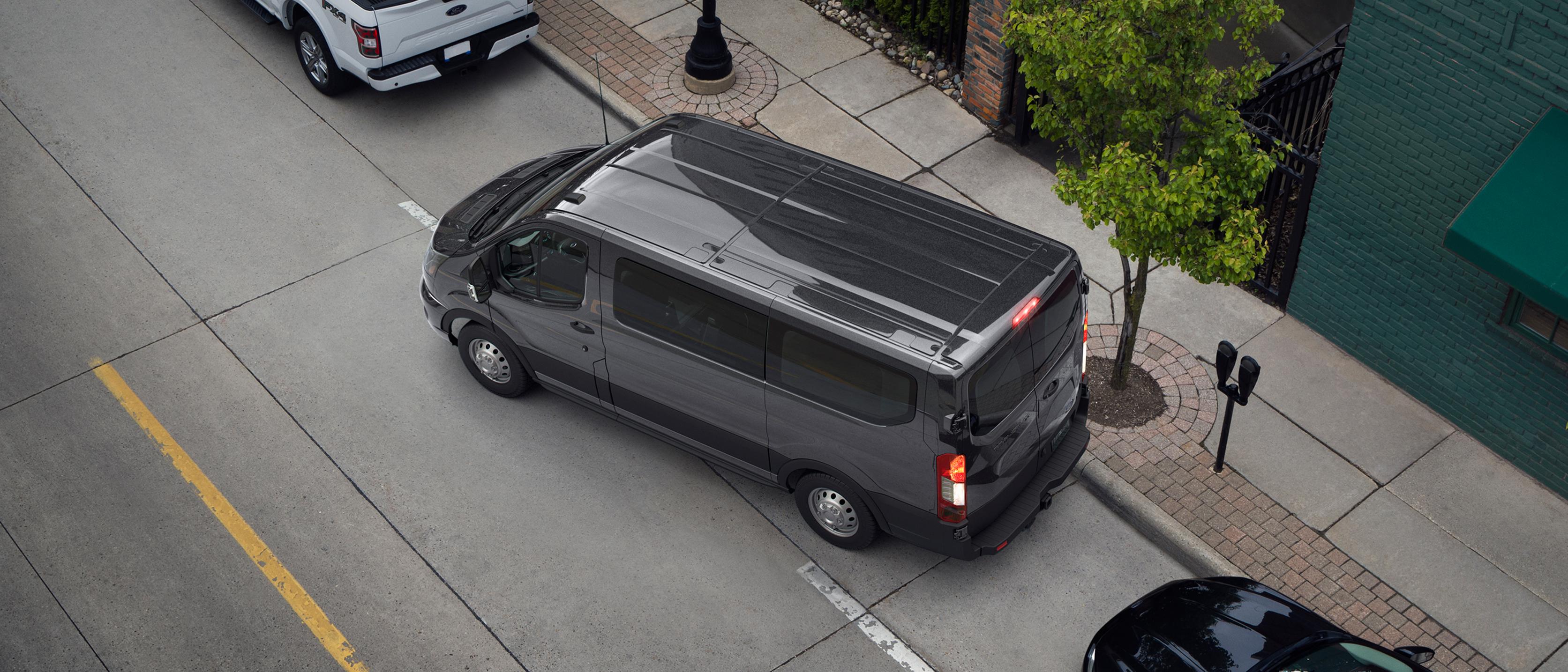 Overhead view of a dark grey 2027 Ford Transit® Van parallel parking on a city street between other vehicles