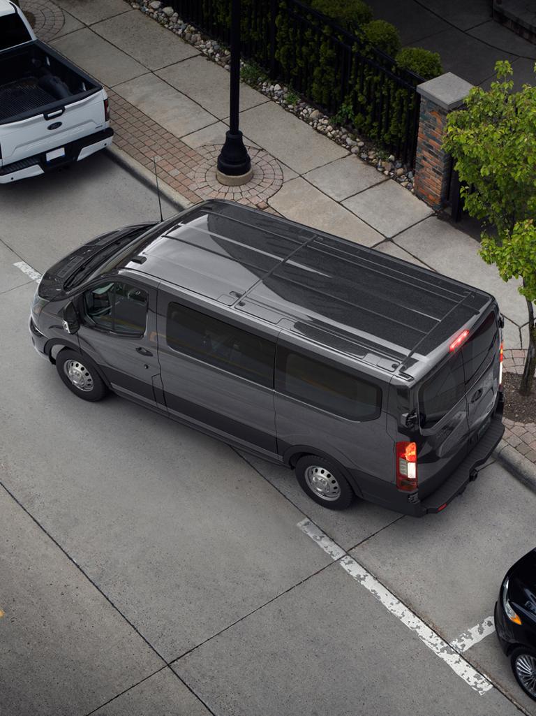 An aerial view of a dark grey 2027 Ford Transit® Passenger Van parallel parking on a city street
