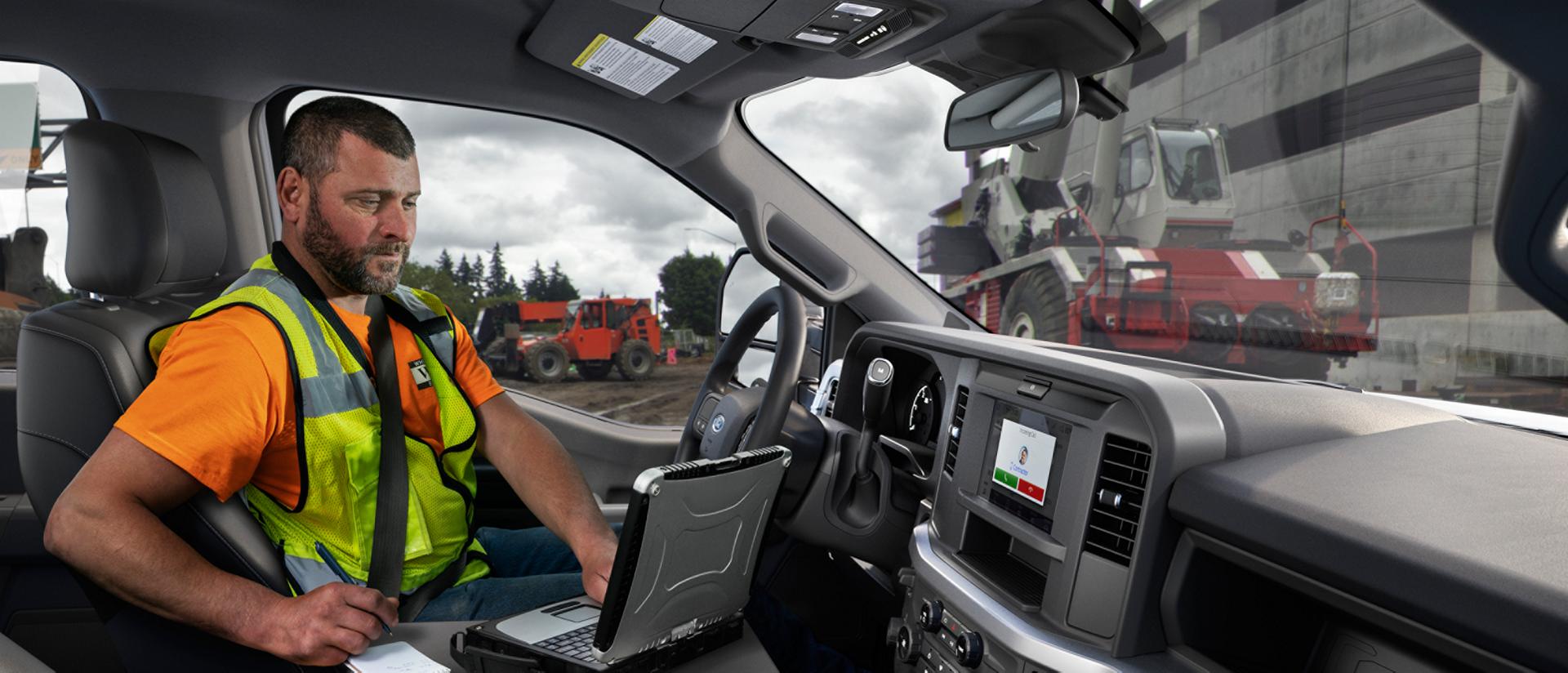 A person inside the cabin of their 2027 Ford Super Duty® truck using a laptop with the interior work surface