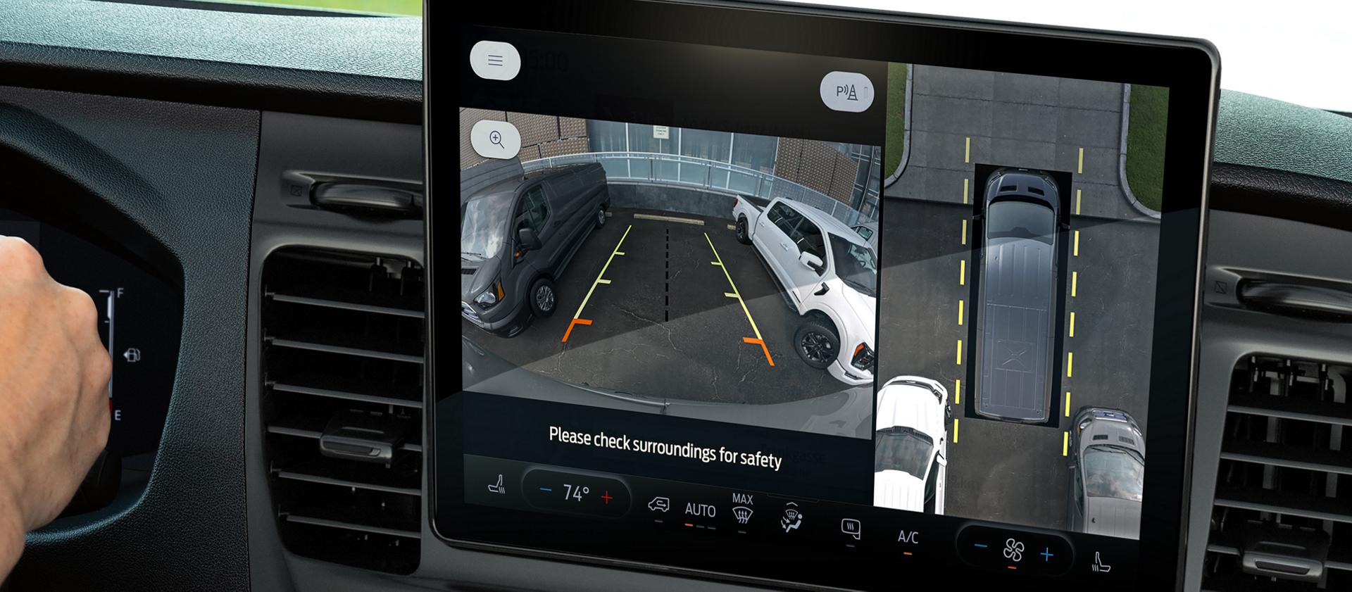 Dashboard display with a parking camera view showing guidelines and surrounding vehicles, and a hand on the steering wheel