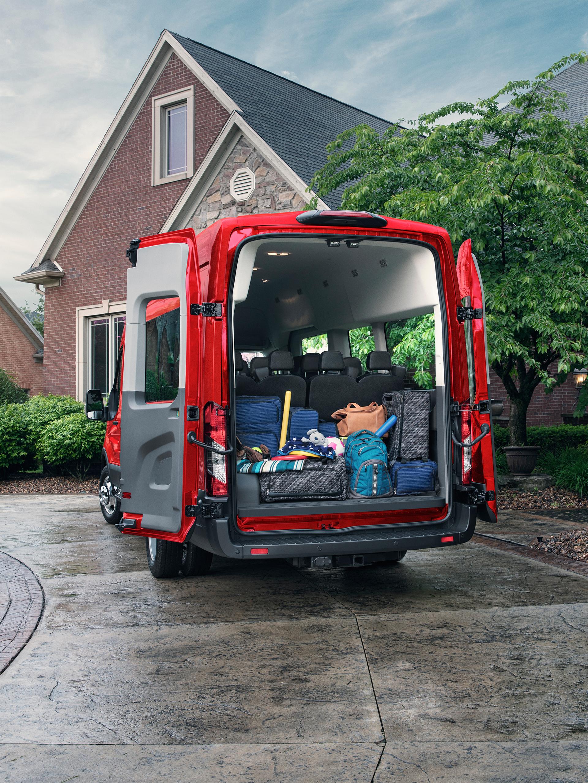 A Red 2027 Ford Transit® Van with open rear doors, cargo area filled with various items, parked at a house