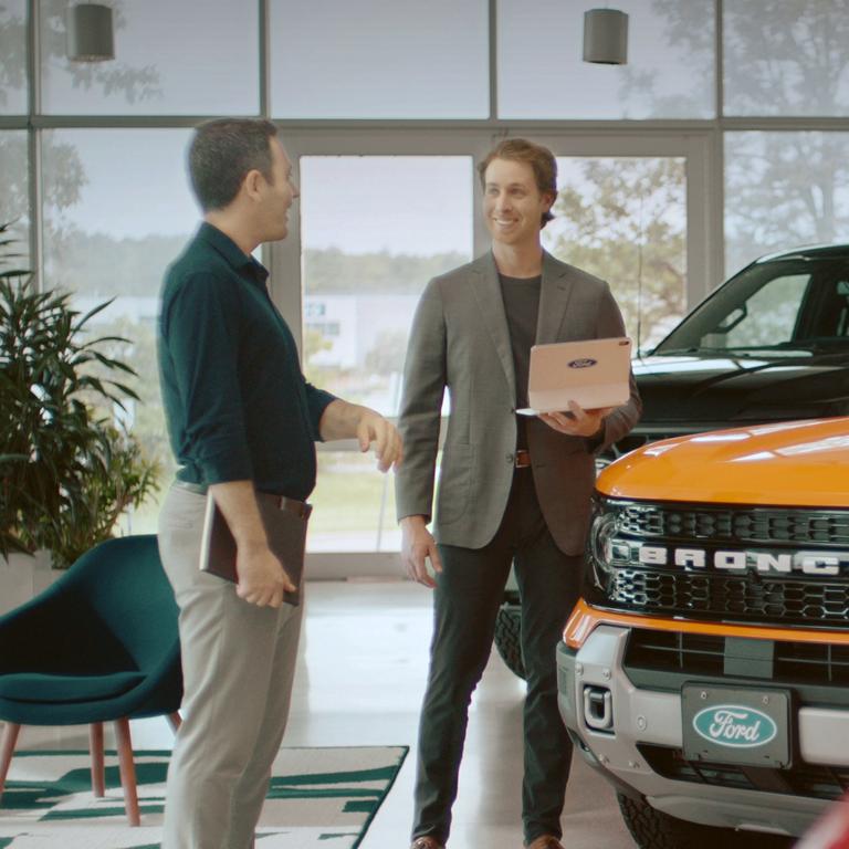 Two people converse next to a Ford vehicle.