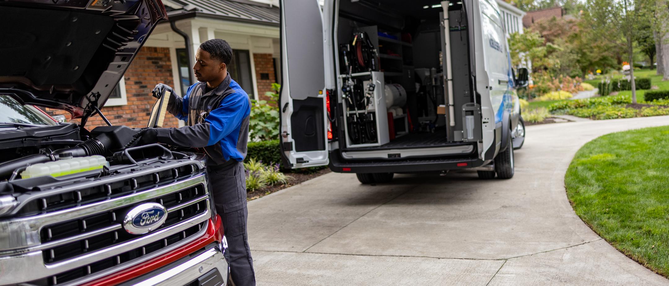 A Ford Service technician works on a vehicle. The Mobile Service work truck is in the background.