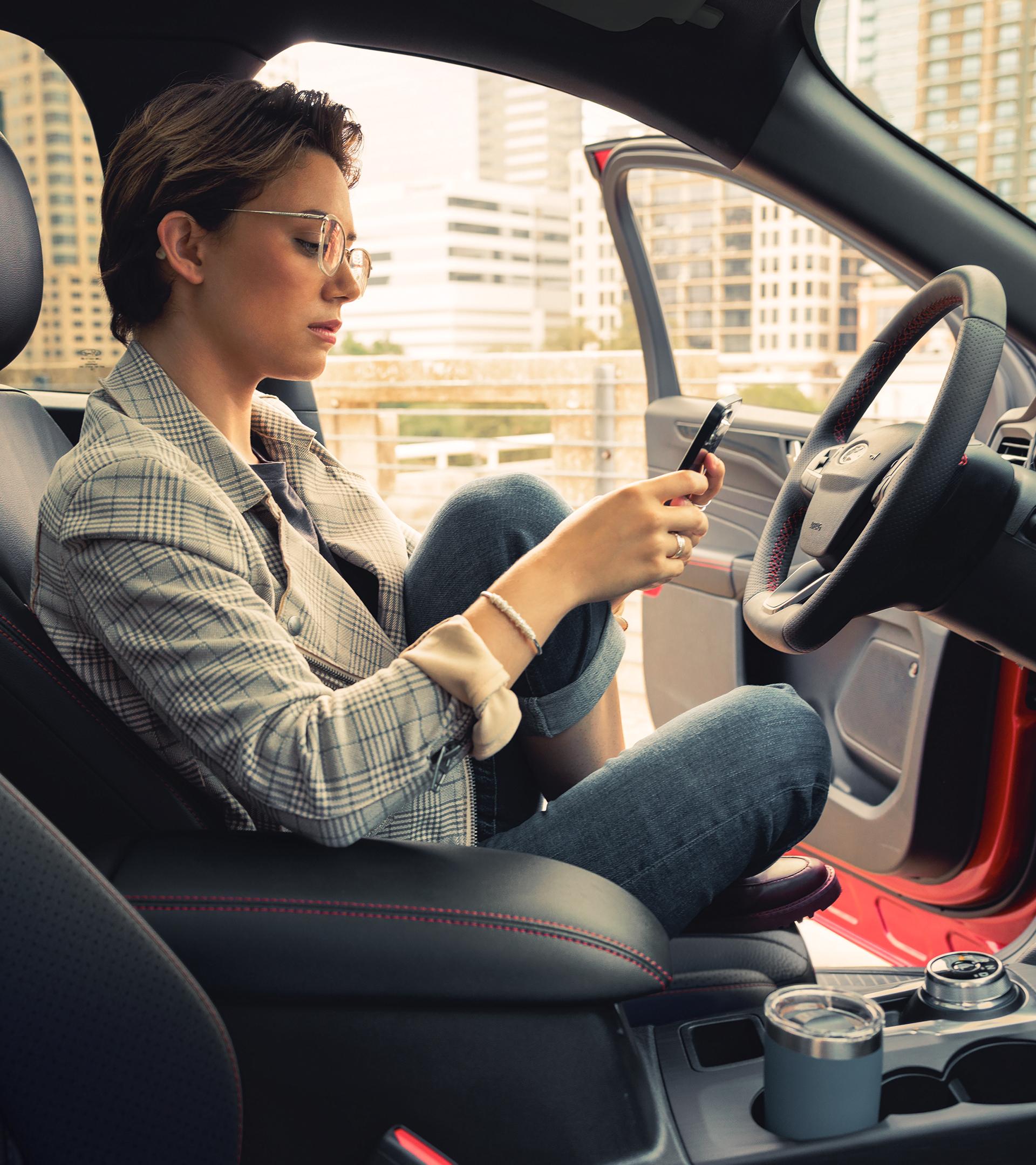 Person sitting in the driver’s seat of a Ford vehicle using a smartphone.