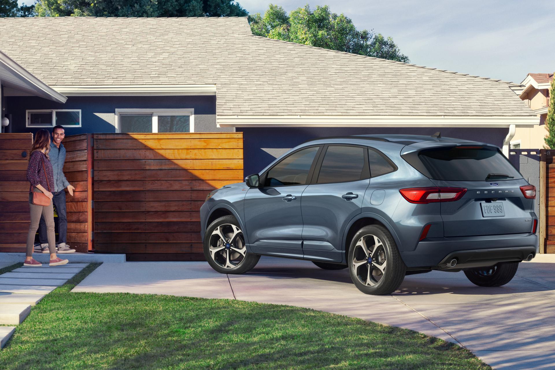 Two people walk towards a Ford vehicle parked in a driveway.