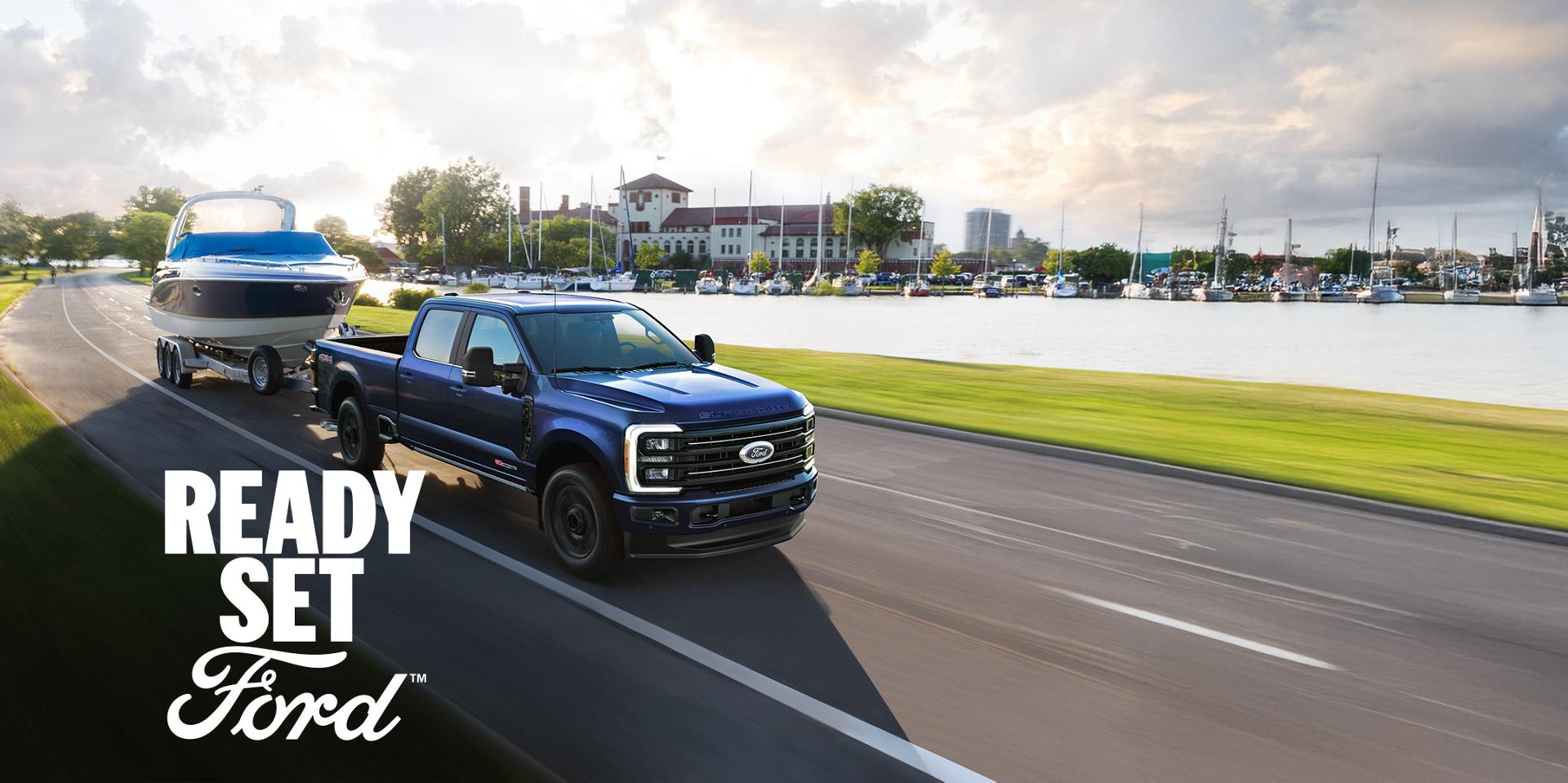 A blue 2026 Ford Super Duty towing a boat. White text “Ready Set Ford” is in the lower right corner