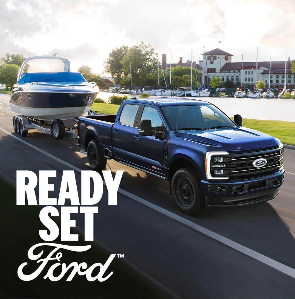 A blue 2026 Ford Super Duty towing a boat. White text “Ready Set Ford” is in the lower right corner