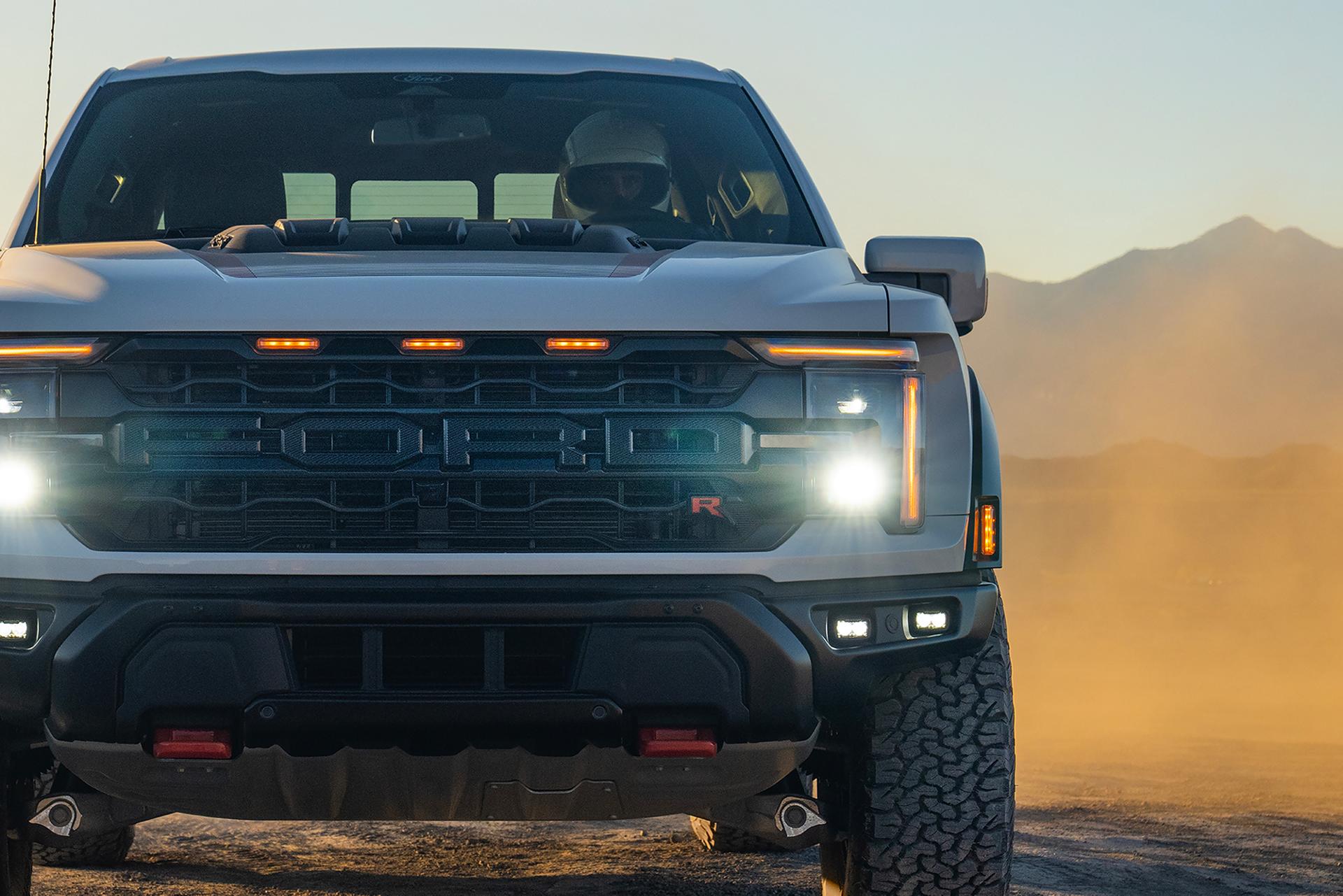 Close-up view of the grille and headlamp on a 2026 Ford F-150® Raptor® model being driven in the desert