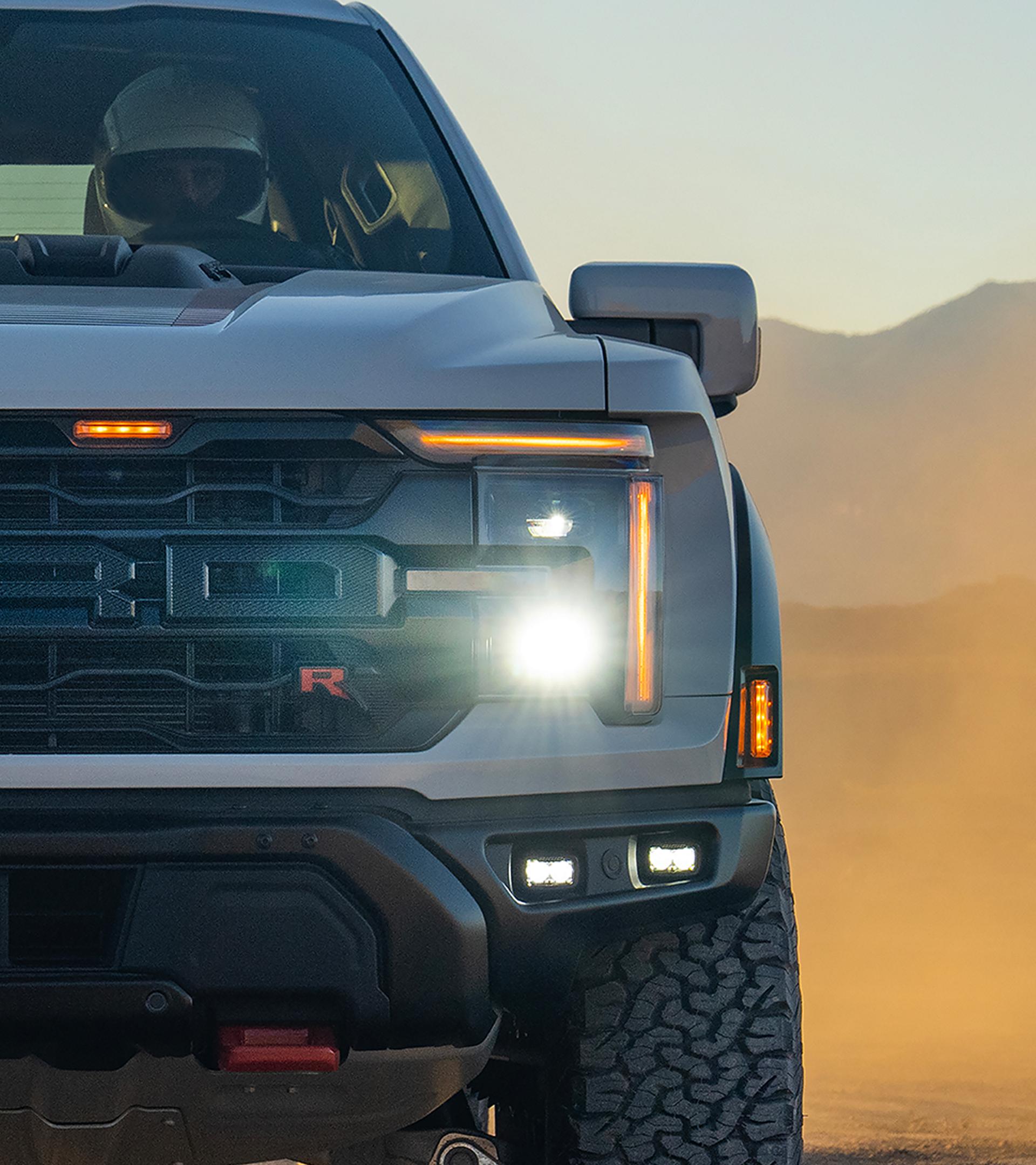 Close-up view on the grille ands headlamp of a 2026 Ford F-150® Raptor® truck being driven in the desert