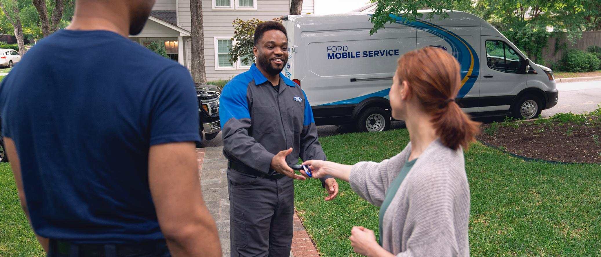 A Ford owner hands their keys to a Ford Mobile Service technician in front of their home.