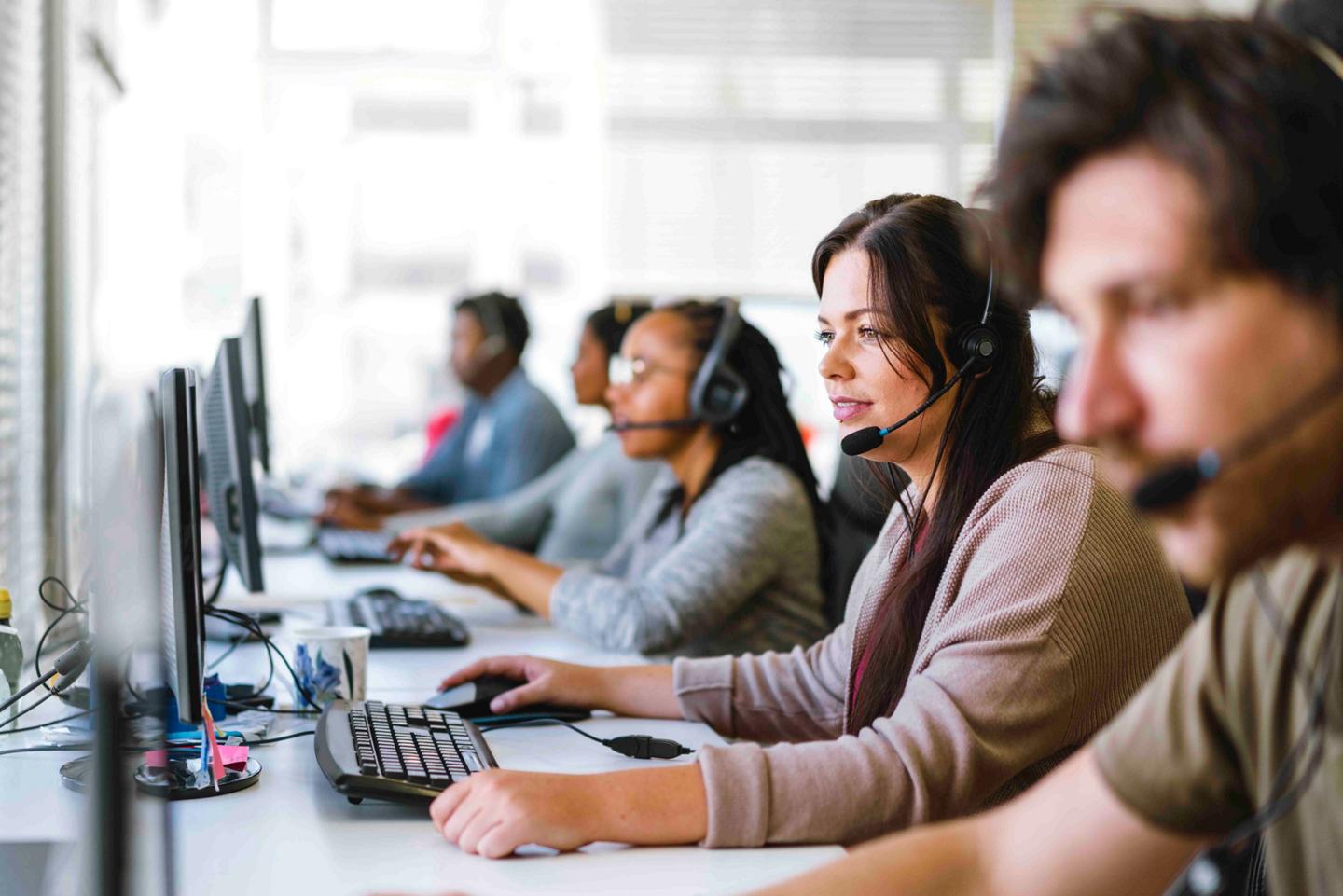 A team of customer service agents, all wearing headsets, seated at a row of computers