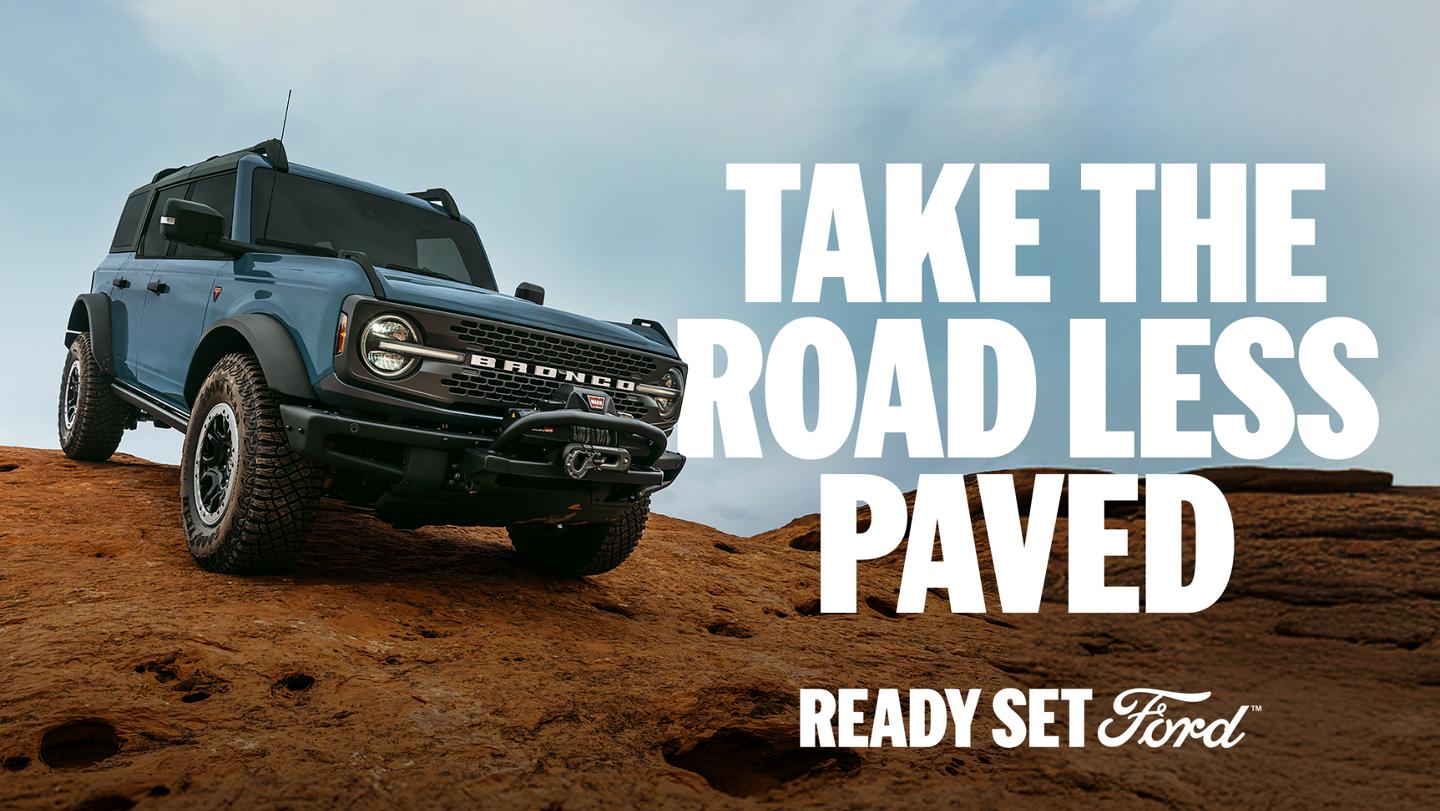 A three-quarter front view of a grey Bronco descending rocky terrain. "Take the road less paved. Ready Set Ford."