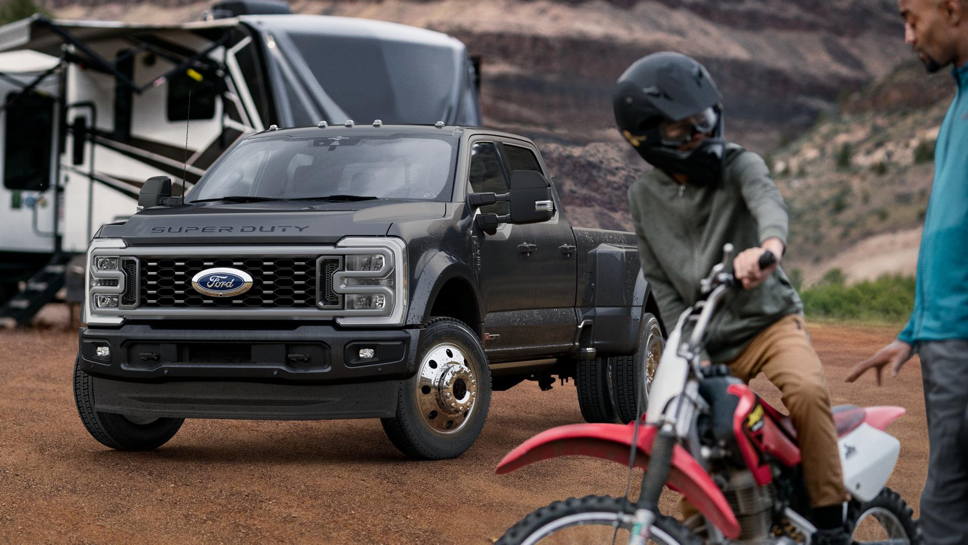 2026 Ford Super Duty® F-450® Platinum® model in Carbonized Grey parked on a campground with campers in the background and a person on a bike in the foreground.