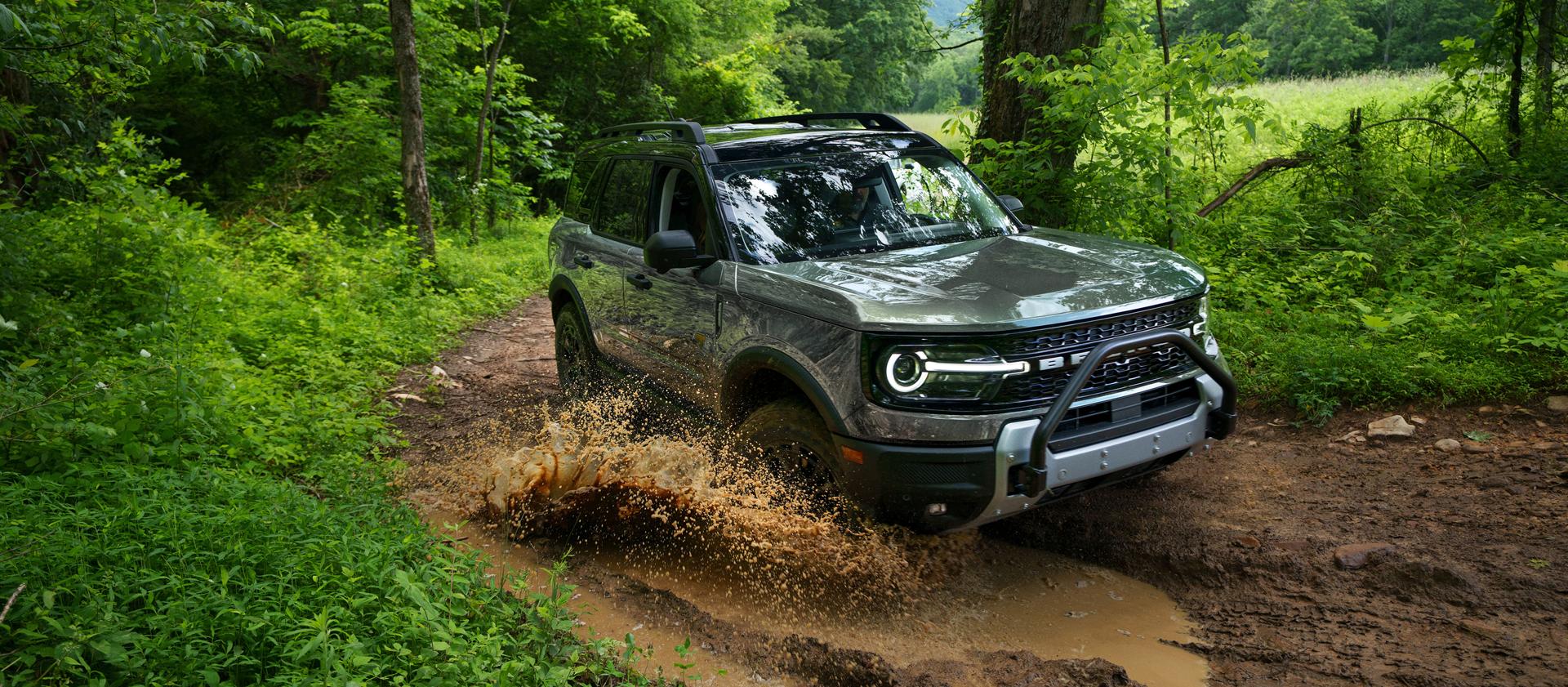 2026 Ford Bronco Sport® being driven on a dirt trail and through a puddle in the woods