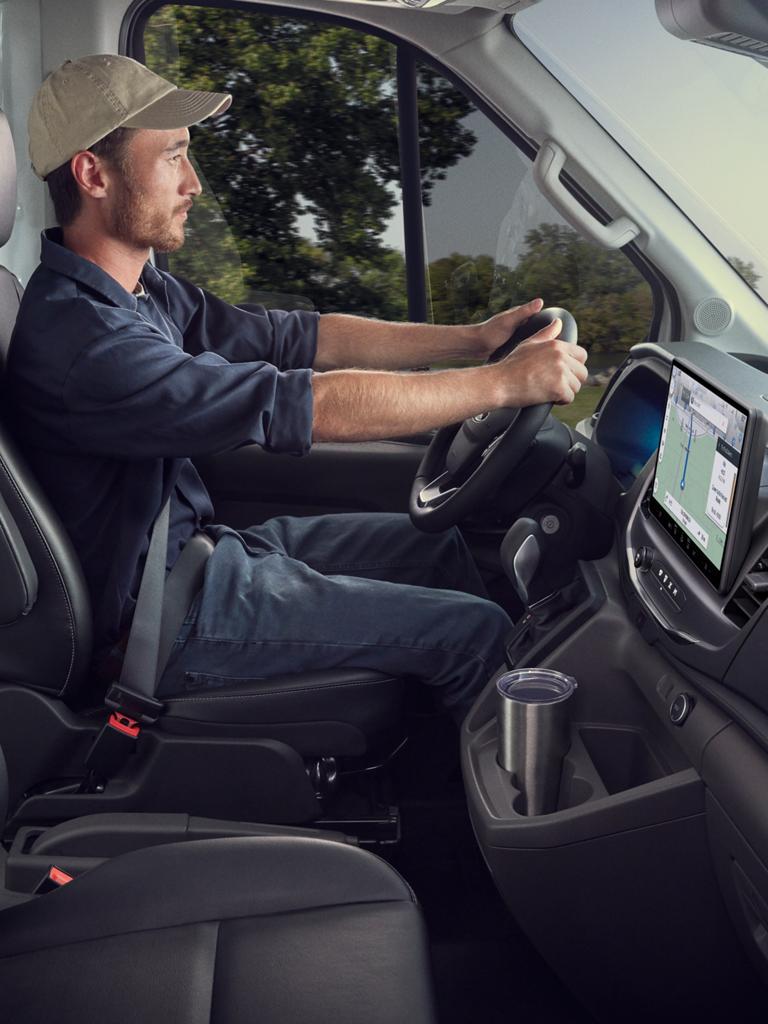 A red 2027 Ford Transit® Cargo Van driving on a wet road in the rain under a dark, stormy sky