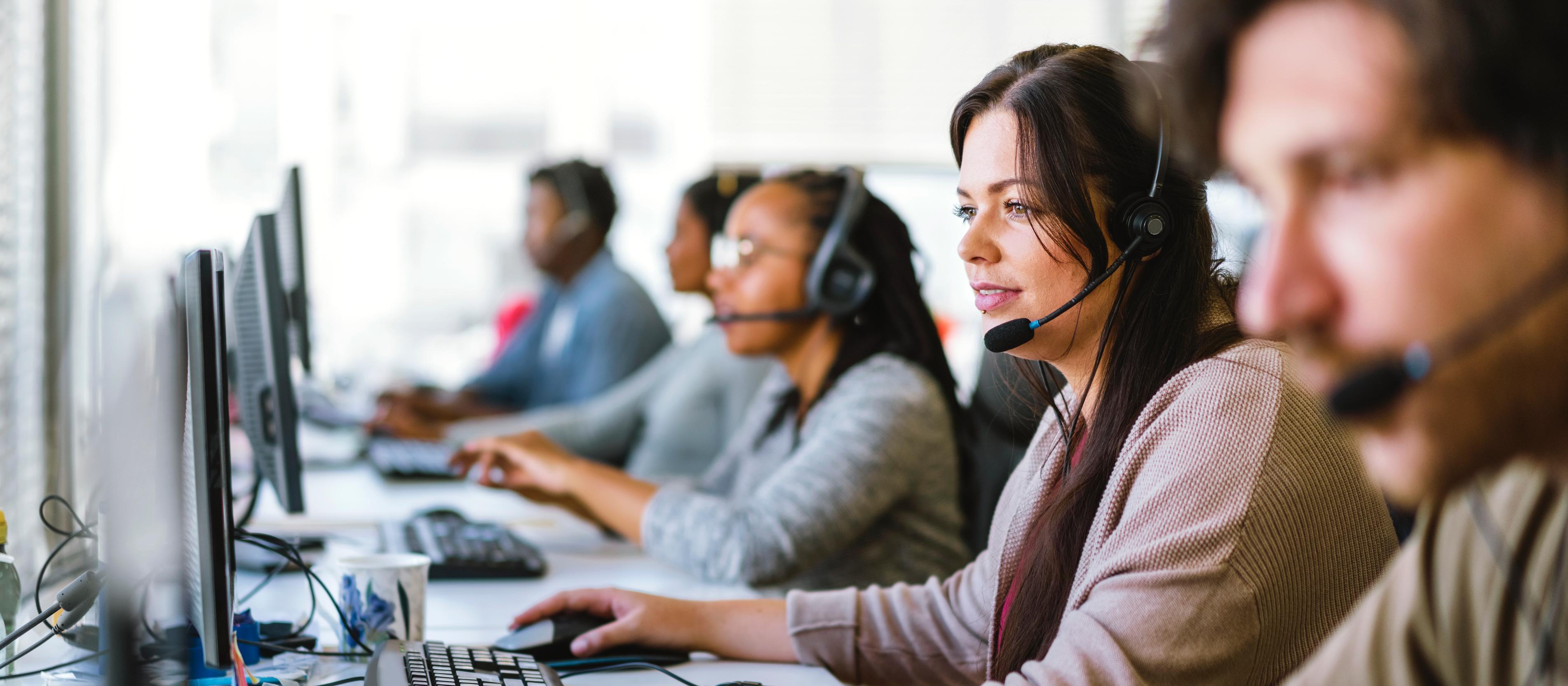 A team of customer service agents, all wearing headsets, seated at a row of computers