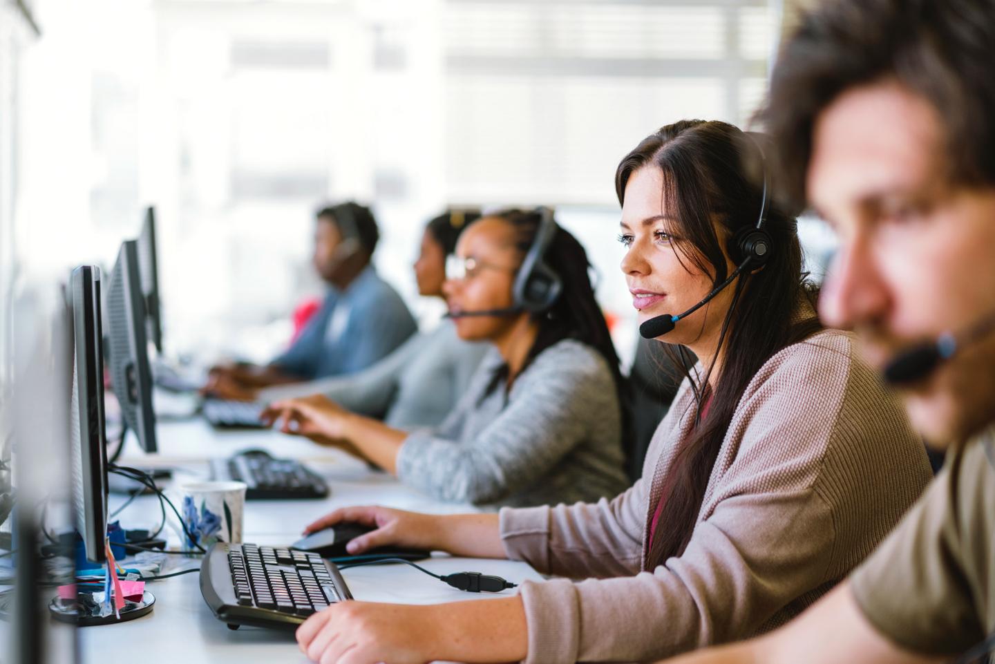 A team of customer service agents, all wearing headsets, seated at a row of computers