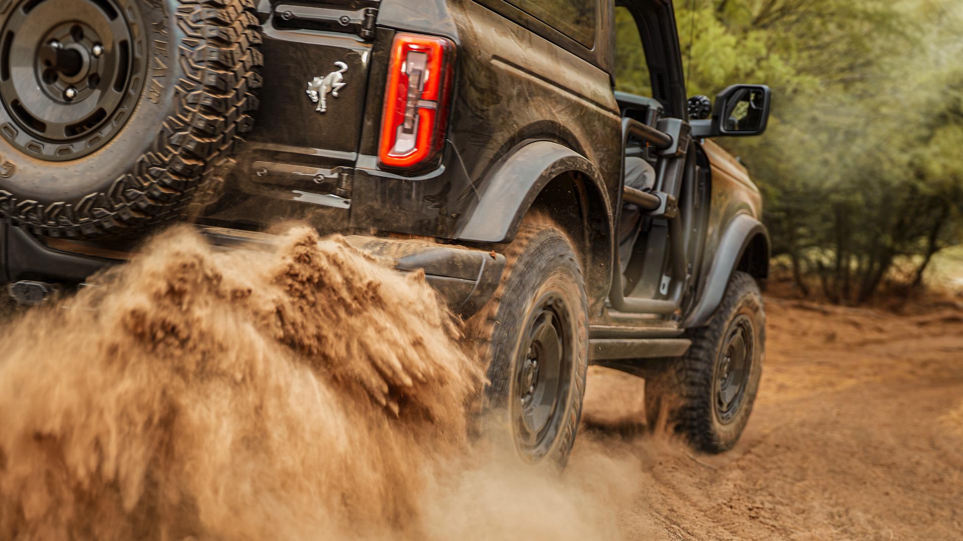 A 2025 Ford Bronco® SUV kicking up mud on a trail in the forest