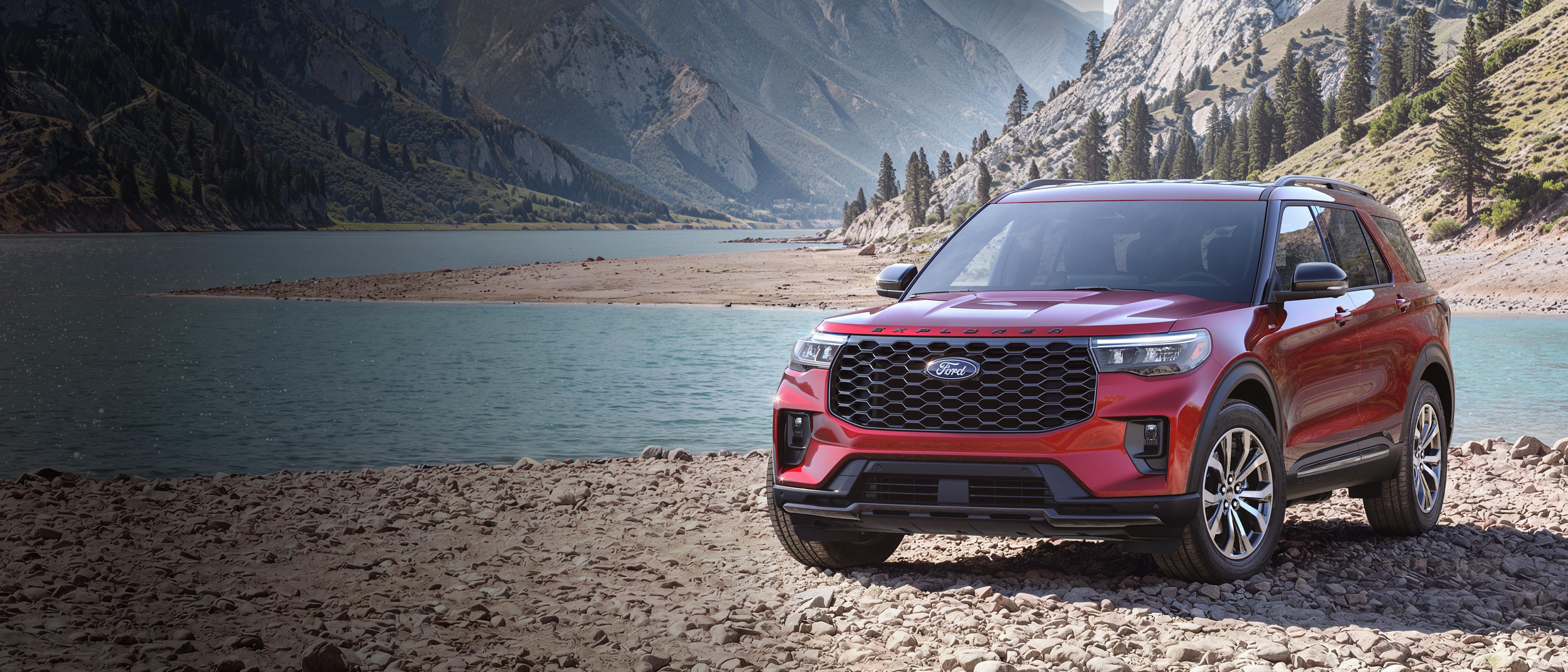 A 2027 Ford Explorer® ST-Line model parked on a rocky expanse near a mountain lake
