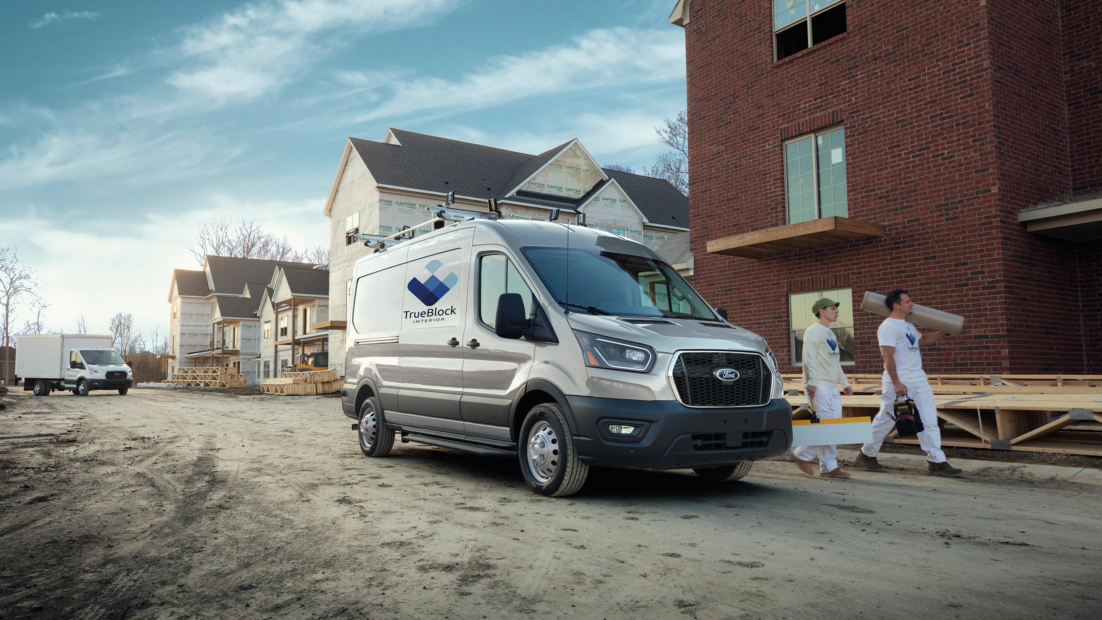 Two workers walking next to a 2026 Ford Transit® van parked in a development