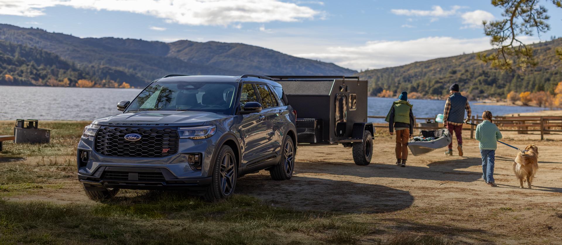 A family and their dog carrying recreational equipment as they walk away from a 2026 Ford Explorer® SUV