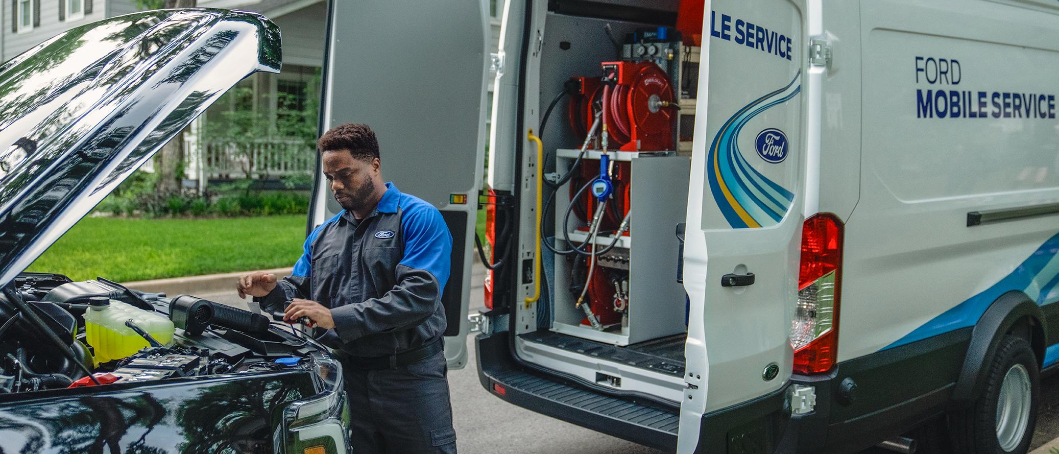 A Ford Mobile Service tech works under the hood of a Ford truck with the open doors of the Mobile Service van behind them.