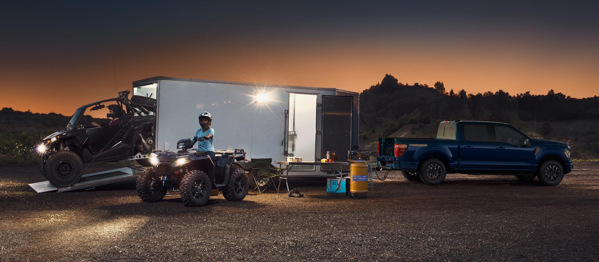 Boy riding an ATV near a 2026 Ford F-150®  Tremor® model hitched to a large trailer at night