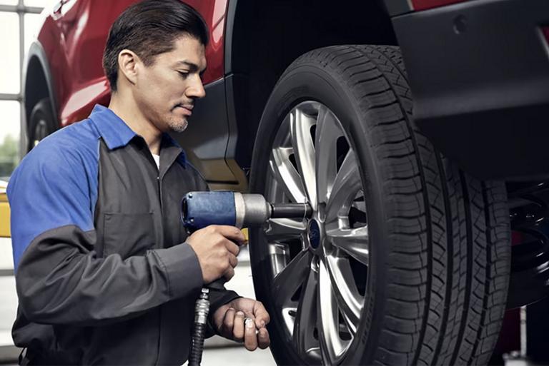 A Ford service tech removes the lug nuts from a Ford vehicle on the lift in the shop